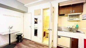 Cocina compacta con pileta, estufa y alacenas. Se ve una pequeña mesa de comedor y una silla.