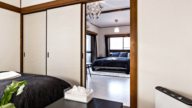 A traditional Japanese-style bedroom with sliding doors, a bed with dark bedding, and a bedside table with a tissue box. - Ikebukuro Yamase Building GR1 (Tokyo)