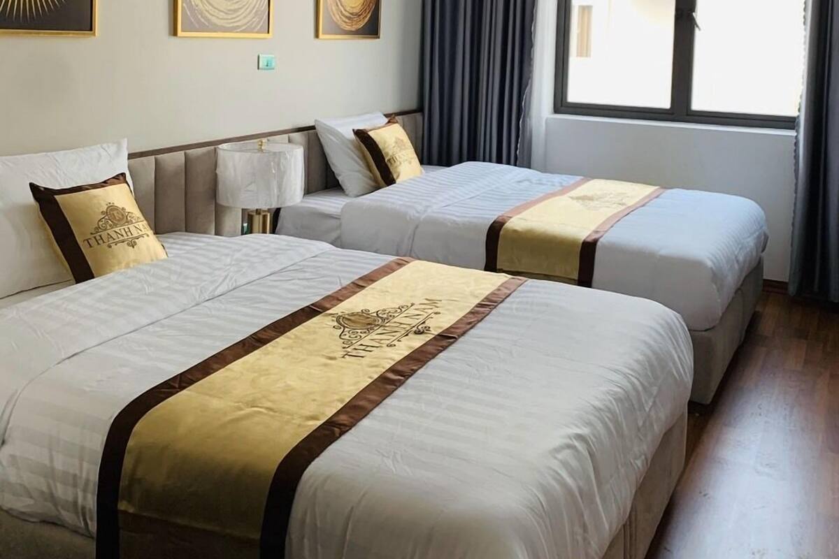 A hotel room with two beds, a large window with curtains, and three wall-mounted artworks.