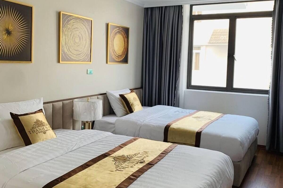 A hotel room with two beds, a window with curtains, and three wall-mounted artworks.