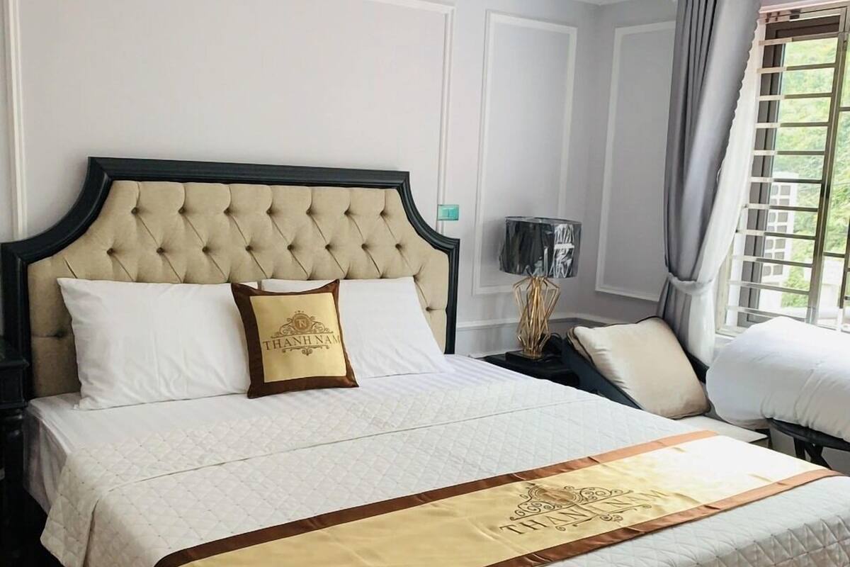 A large bed with a tufted headboard, white bedding, and a decorative gold accent.