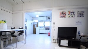 A modern kitchen with white cabinets, a dining area with a glass table and chairs, a flat-screen TV, and artwork on the wall. - RESIDENTIAL HOTEL DAIICHI-H SHIN-OKUBO Room.A (Tokyo)