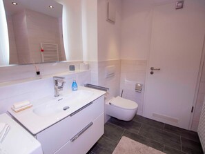 Un baño moderno con lavamanos, espejo y inodoro blancos.