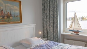 Une chambre avec deux lits, un tableau représentant des voiliers, une fenêtre ornée d’une maquette de voilier et une table de chevet avec une lampe.