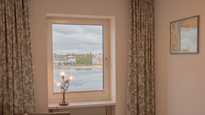 Une chambre avec une fenêtre donnant sur une rivière, un radiateur placé sous la fenêtre et un tableau encadré accroché au mur.