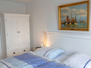 Un dormitorio con una cama, una mesita de noche, un armario blanco y un cuadro de veleros en la pared.
