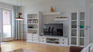 Un salon avec un téléviseur, des meubles blancs, une bibliothèque et un coin repas.
