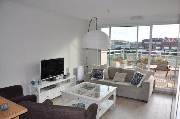 A modern living room with a television, sofa, coffee table, and large windows offering a view of the city.