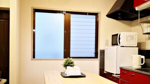 Eine kleine Küche mit einem Holztisch, vier weißen Hocker, einer Mikrowelle und einem roten Schrank.