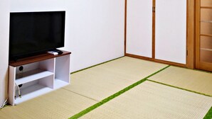 Ein Zimmer mit Tatami-Böden, einem Fernseher auf einem Schrank und einer Schiebetür.