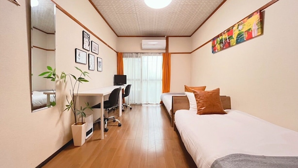 Una camera d'hotel con un letto, una scrivania, una sedia, uno specchio, una pianta e un quadro appeso al muro.