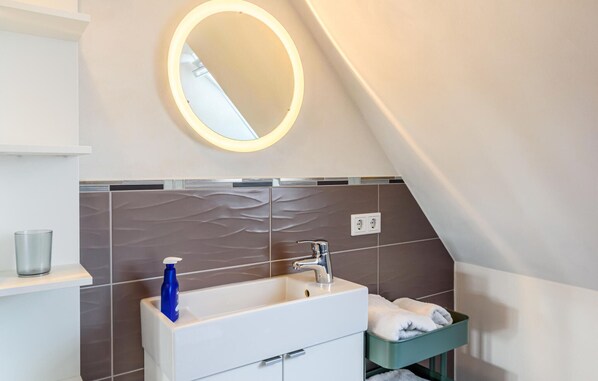 Un baño con un lavamanos blanco, un espejo con luz, un perchero y un estante verde.