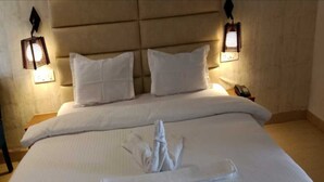 Habitación de hotel con una cama grande, dos almohadas, una toalla doblada con cuidado y dos lámparas fijadas a la pared.