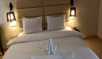 Habitación de hotel con una cama grande, dos almohadas, una toalla doblada con cuidado y dos lámparas fijadas a la pared.