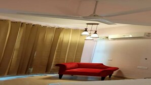 Una habitación de hotel con una cama, una silla roja, un ventilador de techo y una ventana con cortinas.
