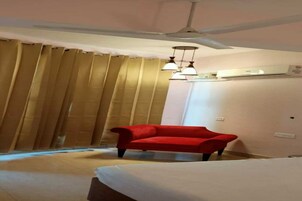 Una habitación de hotel con una cama, una silla roja, un ventilador de techo y una ventana con cortinas.