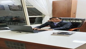 Un hombre sentado en un escritorio con una computadora portátil, un ratón y un cuaderno.