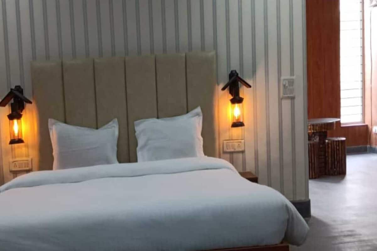 Uma cama com lençóis brancos, duas luminárias fixadas na parede e uma cabeceira de madeira.