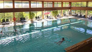 En inomhuspool med klart vatten, solstolar och utsikt över grönområden utanför.