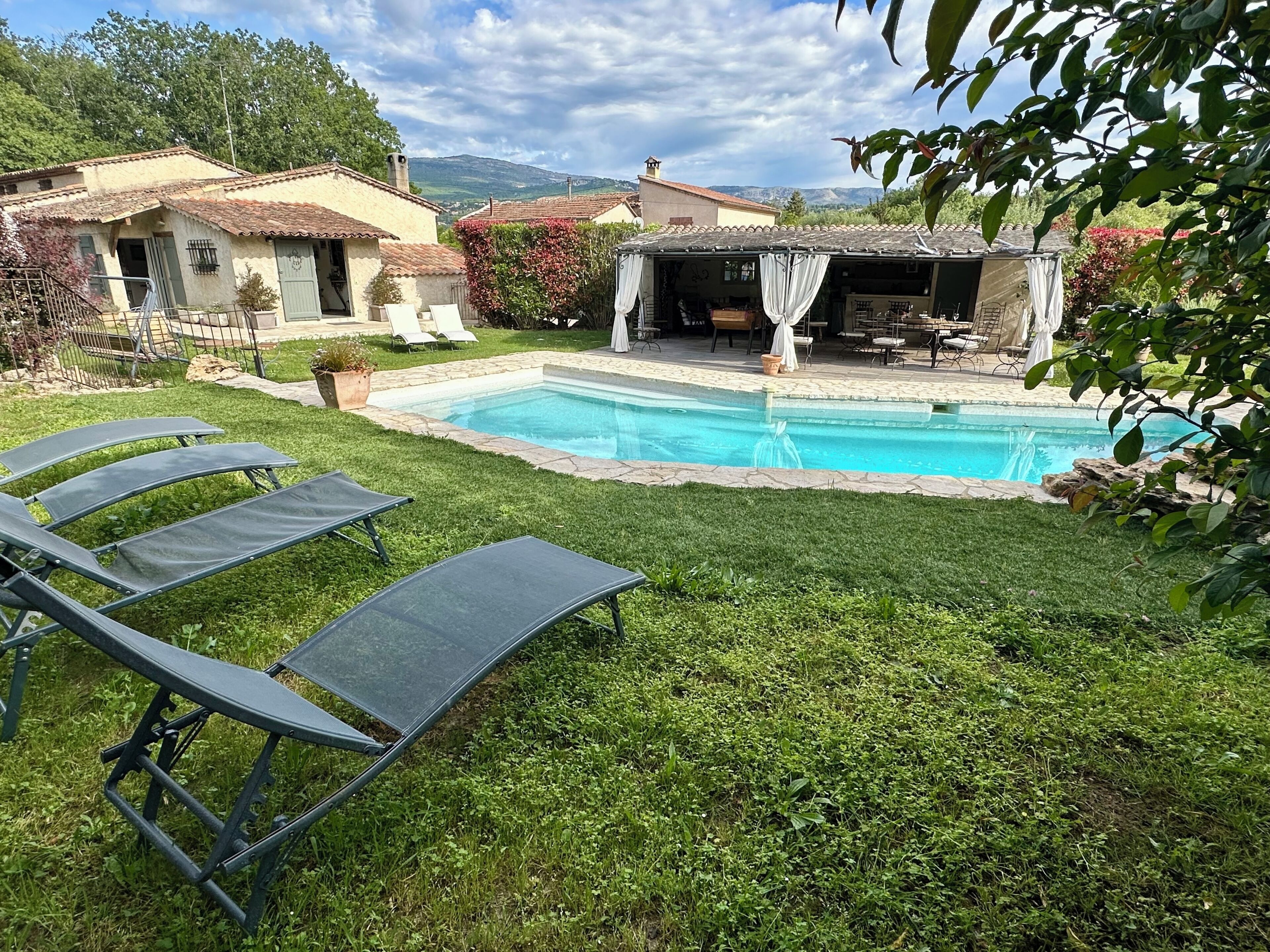 A backyard with a swimming pool, lounge chairs, and a patio area with outdoor furniture.