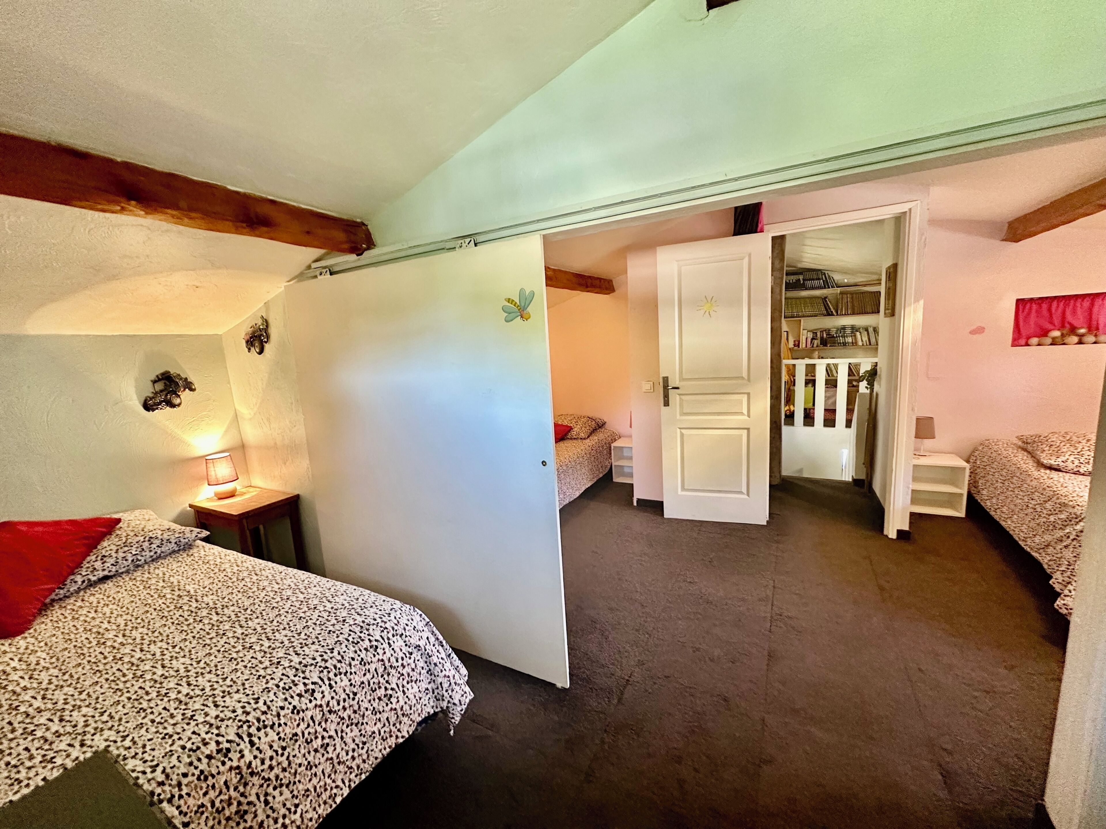 A bedroom with two beds, a wardrobe, and a small table with a lamp.