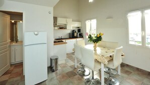 A modern kitchen with white cabinets, a refrigerator, and a dining area with a table and chairs. - 50m from the beach, 2 apartments side by side, sea view, tip of the Giens peninsula (Hyères)