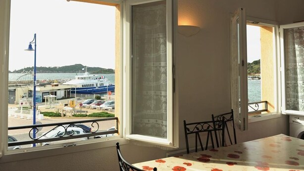 A room with a balcony overlooking a marina, a table with chairs, and a window with a view of boats and hills. - 50m from the beach, 2 apartments side by side, sea view, tip of the Giens peninsula (Hyères)