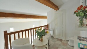 A room with a wooden ceiling, a white door, a white chair, a small round table, and a vase with flowers. - 50m from the beach, 2 apartments side by side, sea view, tip of the Giens peninsula (Hyères)