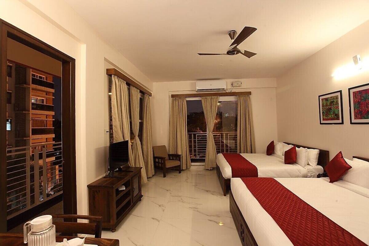 Quarto de hotel com duas camas, televisão, ventoinha no teto e varanda com cortinas.