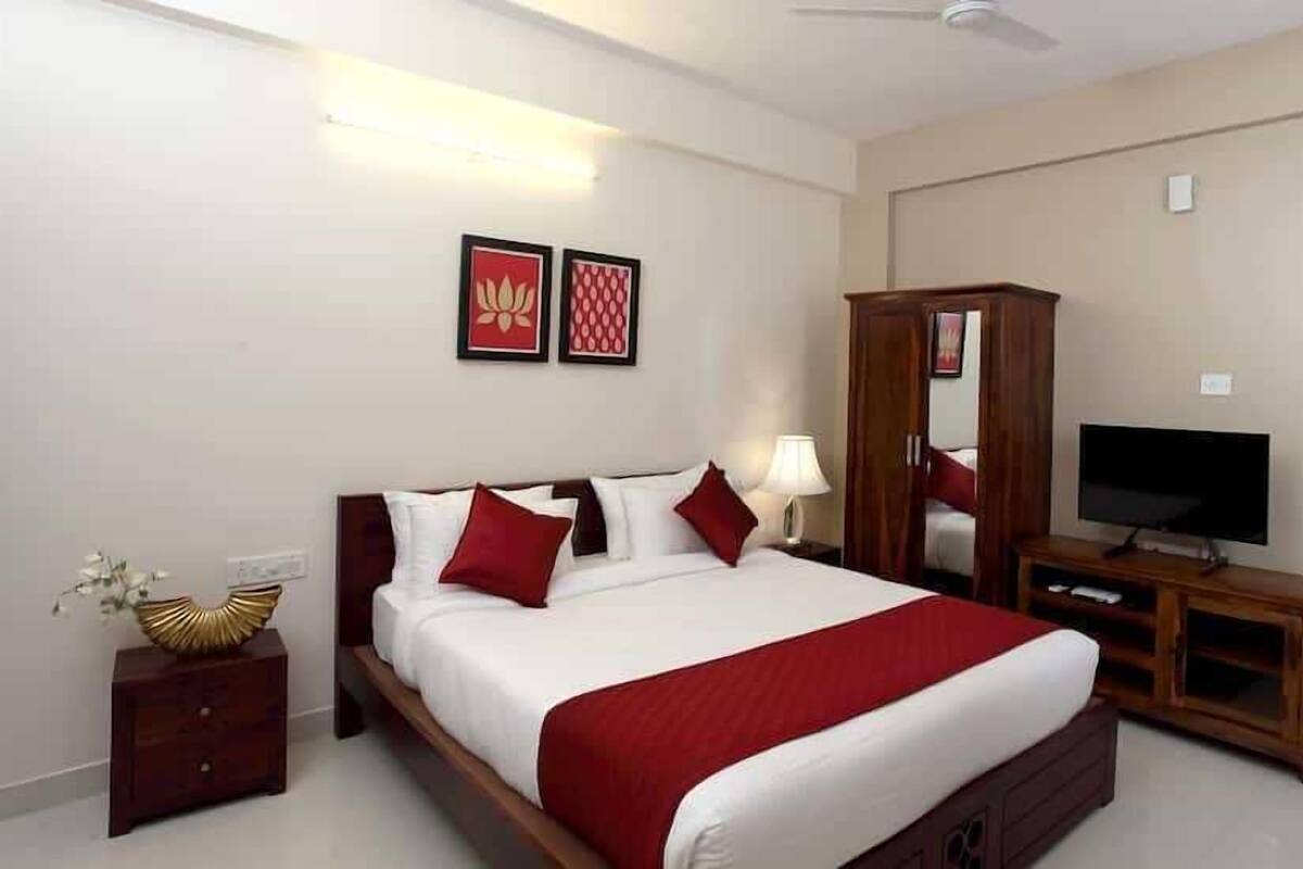 Quarto de hotel com cama, televisão, guarda-roupa e duas imagens emolduradas na parede.