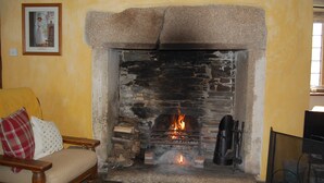 Uma lareira de pedra com fogo, um banco de madeira e um quadro na parede.