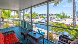 Un espacio exterior techado con mobiliario de mimbre, una mesa de vidrio y vistas a un puerto deportivo con barcos y edificios.