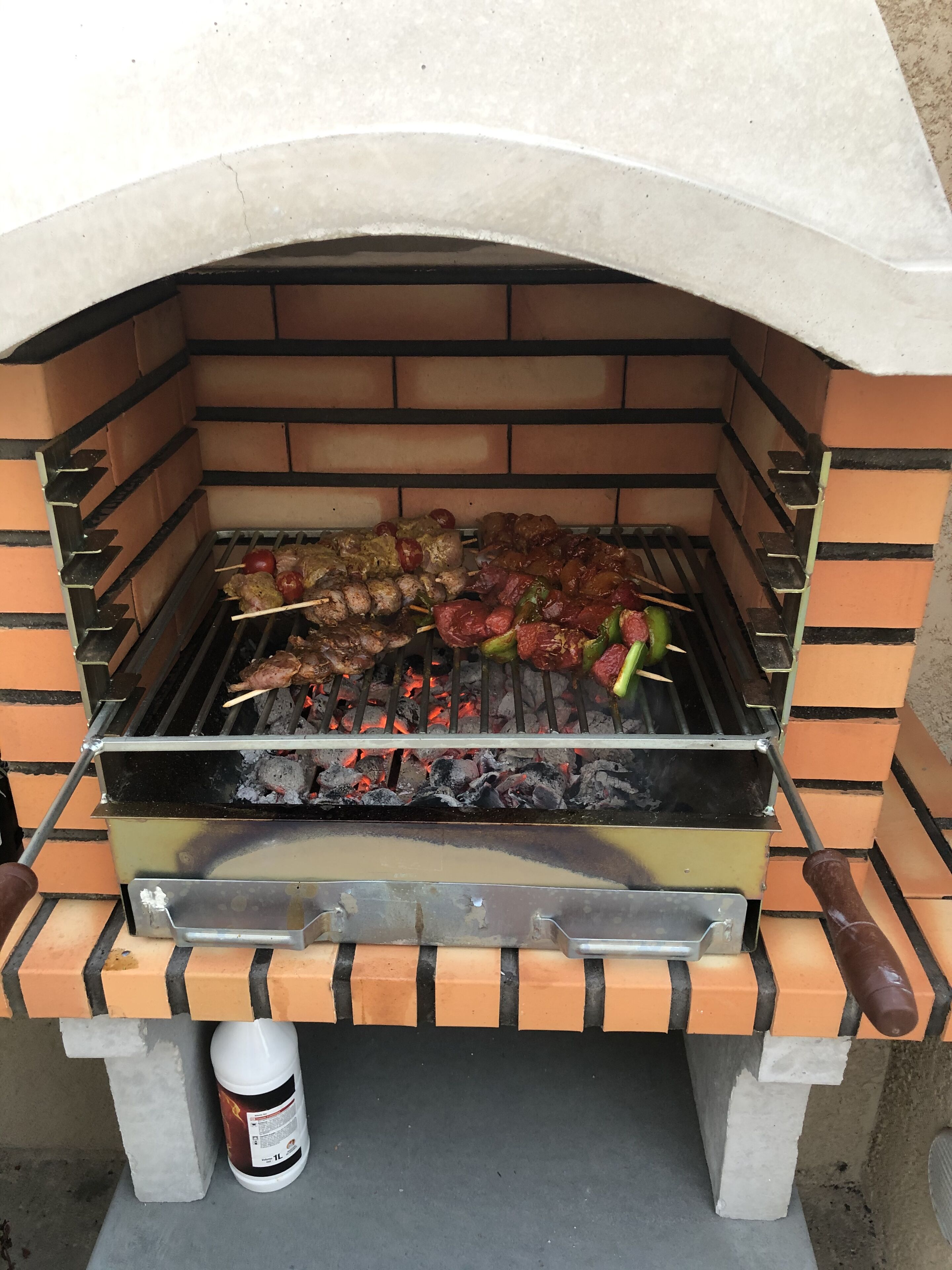 A brick oven grill with skewers of meat and vegetables.