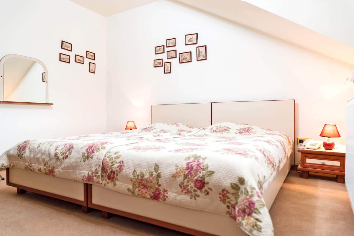 A bedroom with a bed, bedside lamps, a nightstand, a mirror, and framed pictures on the wall.