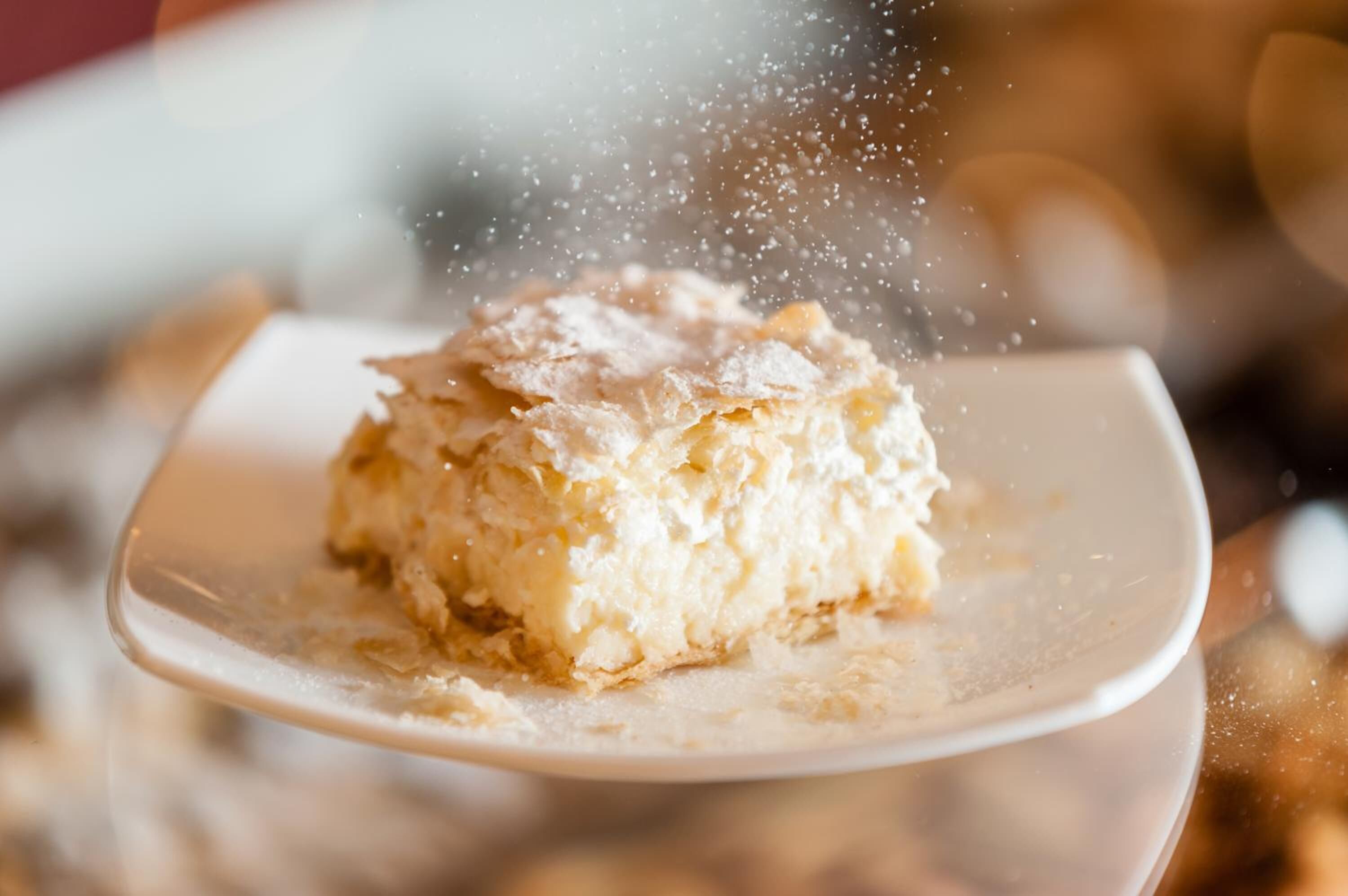 A piece of cake on a plate with powdered sugar being sprinkled on it.