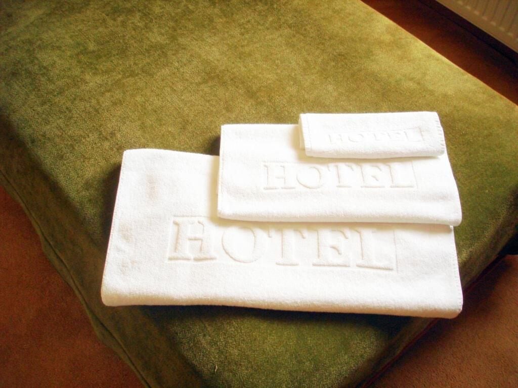 Une pile de serviettes blanches, portant en relief l’inscription « HÔTEL », est posée sur une surface en tissu vert.