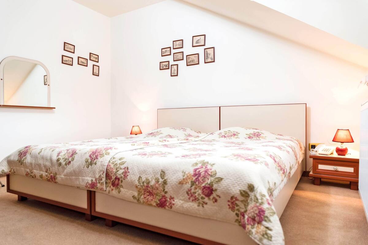 A bedroom with a bed, bedside lamps, a nightstand, a mirror, and framed pictures on the wall.