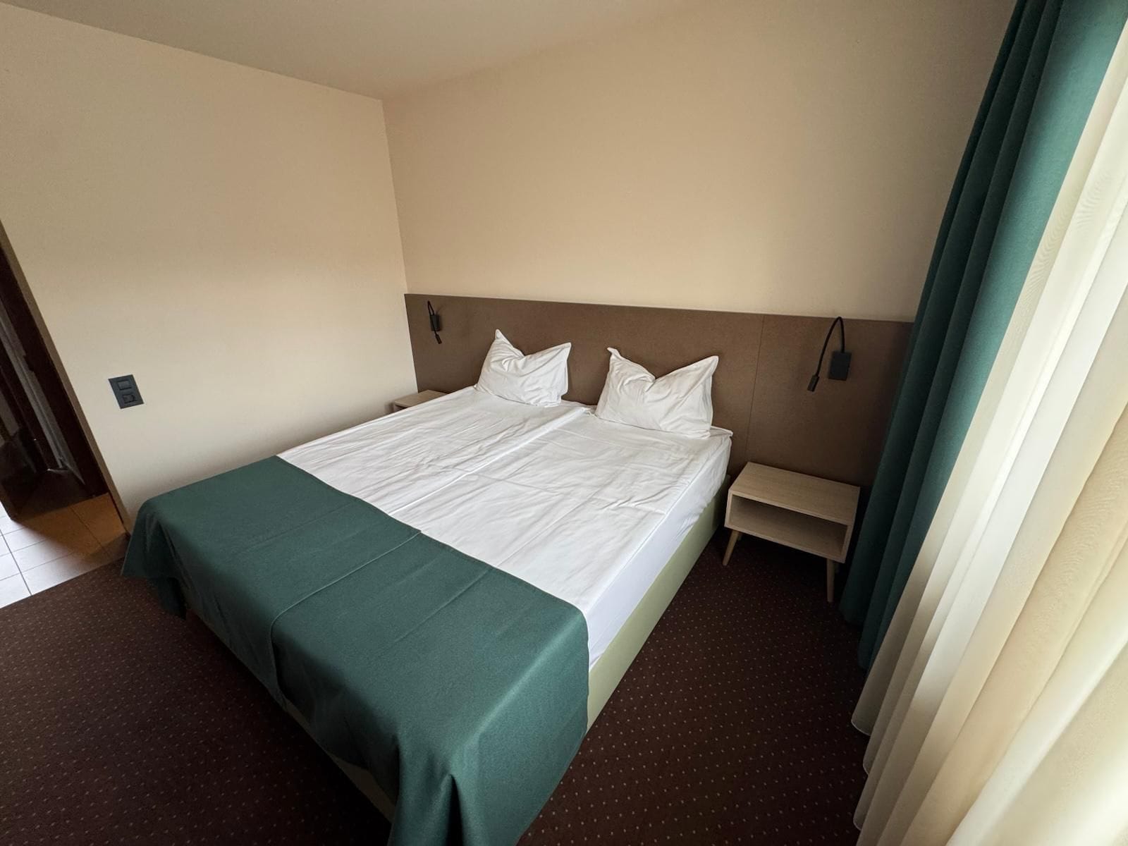 A hotel room with a bed, a bedside table, and a curtain.