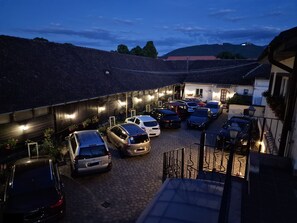 A parking area with multiple cars and a building with a sloped roof. - Pensiunea Luiza (Brasov)