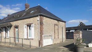 A stone building with a sloped roof, a chimney, and a small garden area with a potted plant. - House Gite 6 persons near Illiers Combray LPE (Magny)