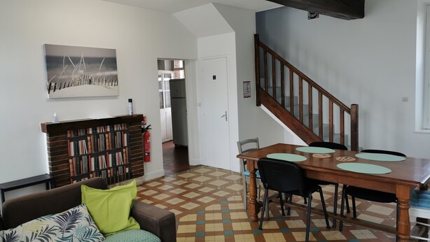 A living room with a wooden dining table, a sofa with patterned cushions, a bookshelf, and a staircase. - House Gite 6 persons near Illiers Combray LPE (Magny)