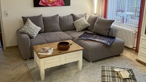Un salon moderne avec un canapé gris, une table basse en bois et un pouf à motifs écossais.