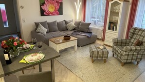 Un salon comprenant un canapé, une table basse, une table à manger ornée d’un vase de fleurs et un buffet.
