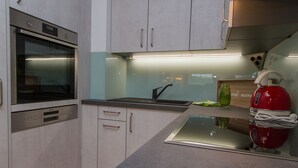 Une cuisine moderne équipée d’appareils électroménagers en acier inoxydable, notamment un four et une bouilloire rouge.