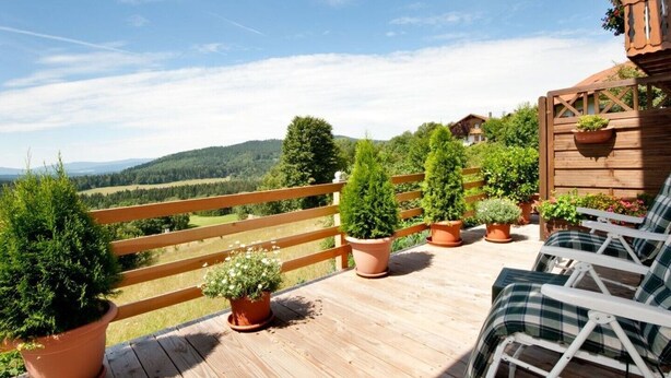 A wooden deck with potted plants, a white chair, and a view of a mountainous landscape.