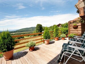 Une terrasse en bois agrémentée de plantes en pot, une chaise blanche et une vue sur un paysage montagneux.