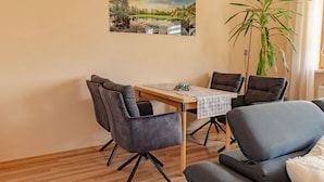 A dining area with a wooden table, six grey chairs, and a large potted plant.