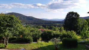 A rural landscape with a house surrounded by trees and a view of distant mountains.