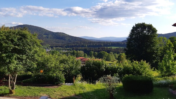 Un paysage rural avec une maison entourée d’arbres et une vue sur des montagnes lointaines.