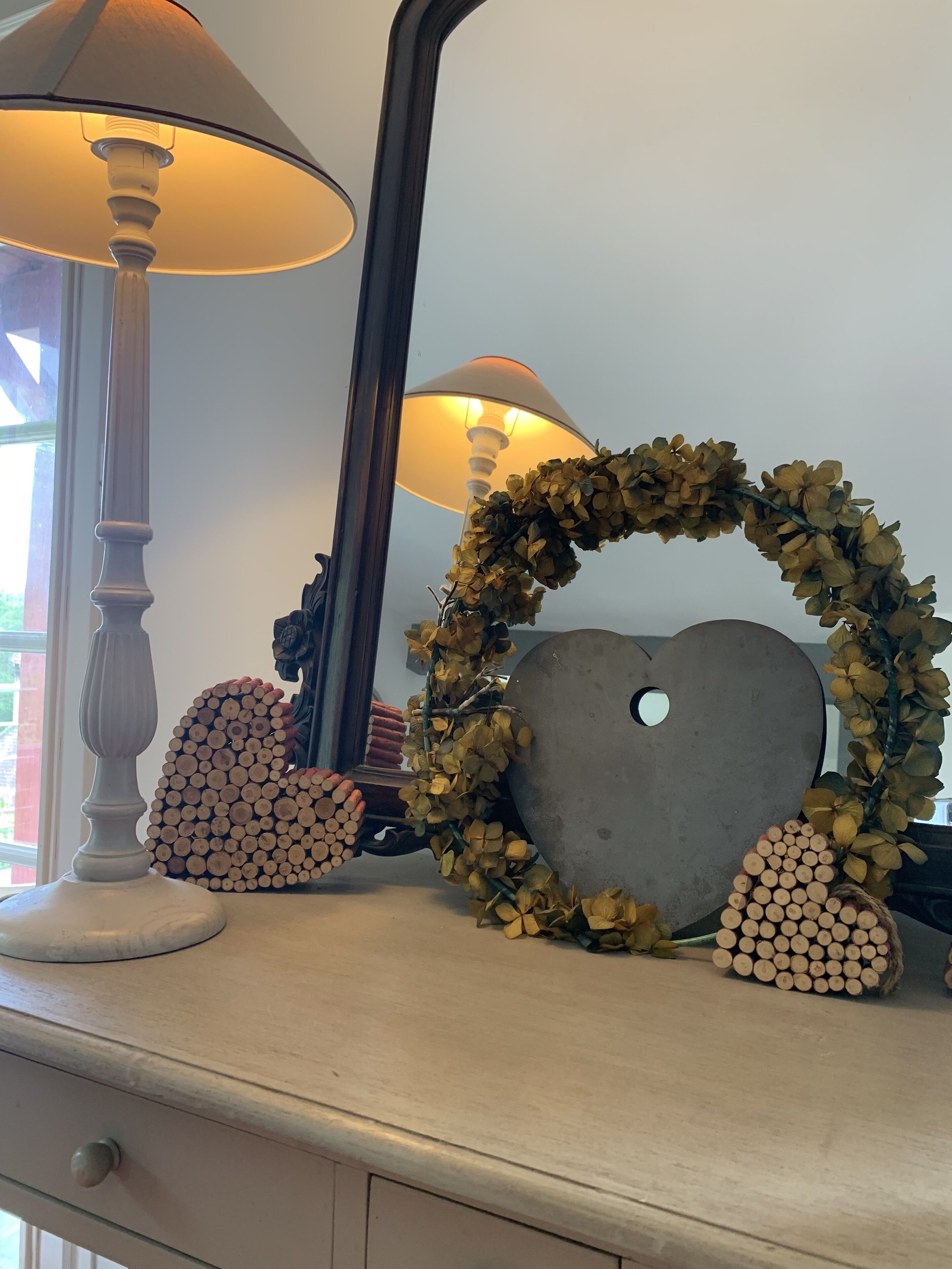 A dresser with a lamp, a heart-shaped decoration, and a mirror.